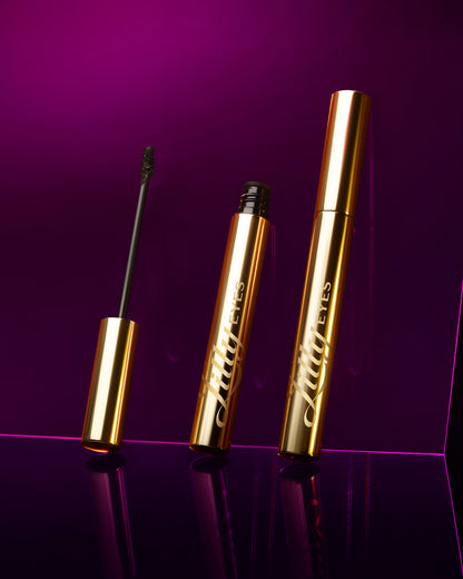 Two gold mascara tubes on a purple background